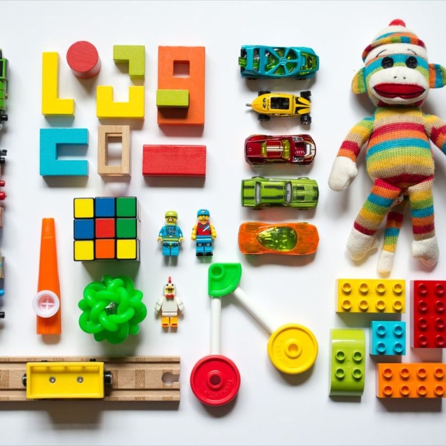 Blocks, toy cars, bricks and a knitted monkey laid out in rows